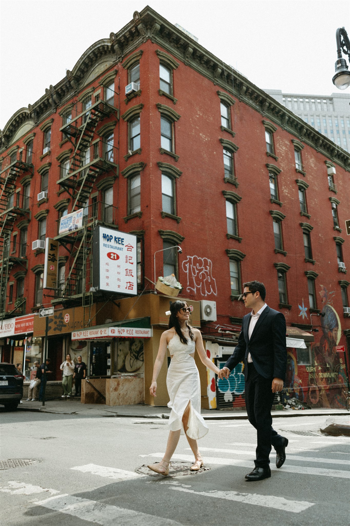 A couple dressed in formal attire affectionately facing each other on a city street corner with buildings in the background as they elope in nyc